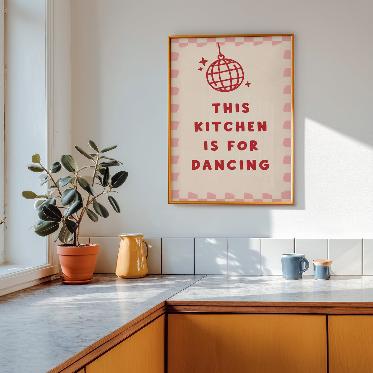Kitchen Is For Dancing pink check print shown in a gold frame above a marble counter with a yellow ceramic jug
