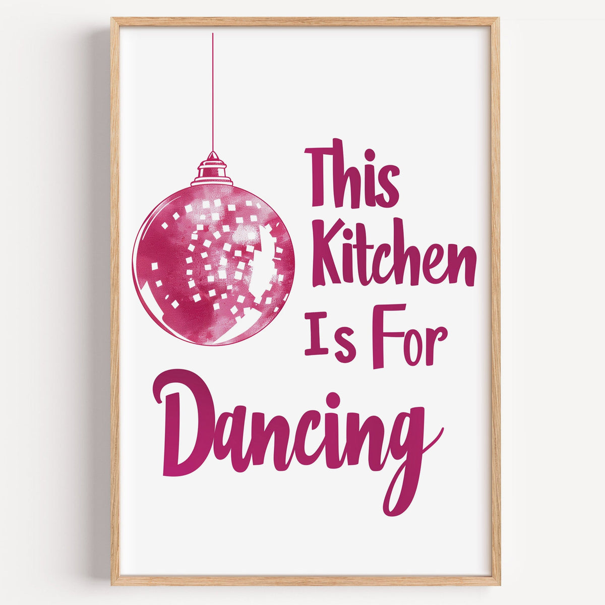 Kitchen Is For Dancing pink script print in a light oak frame on a plain white wall
