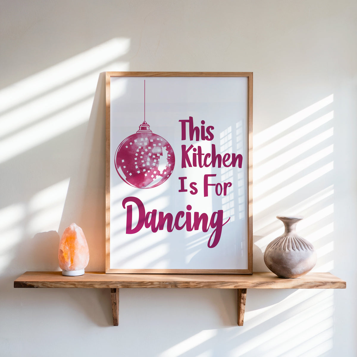 Kitchen Is For Dancing pink script print in an oak frame on a live-edge shelf beside a salt lamp