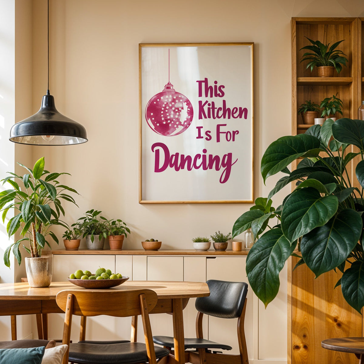 Kitchen Is For Dancing pink script print in an oak frame in a dining room above a plant-lined sideboard