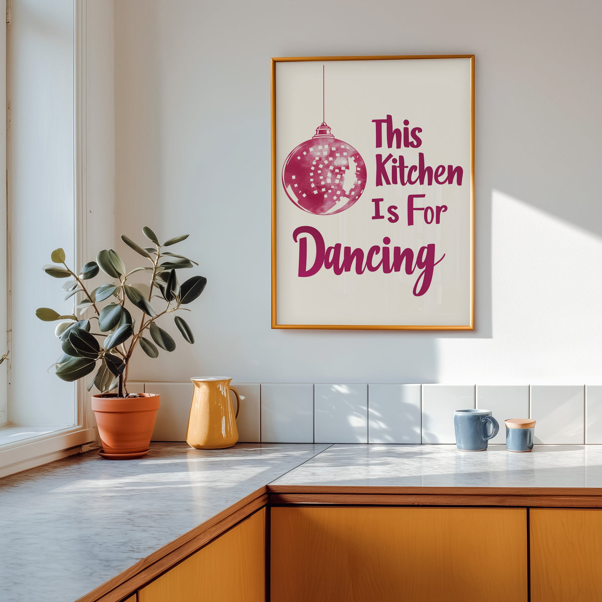 Kitchen Is For Dancing pink script print shown in a gold frame above a marble counter in a tan kitchen