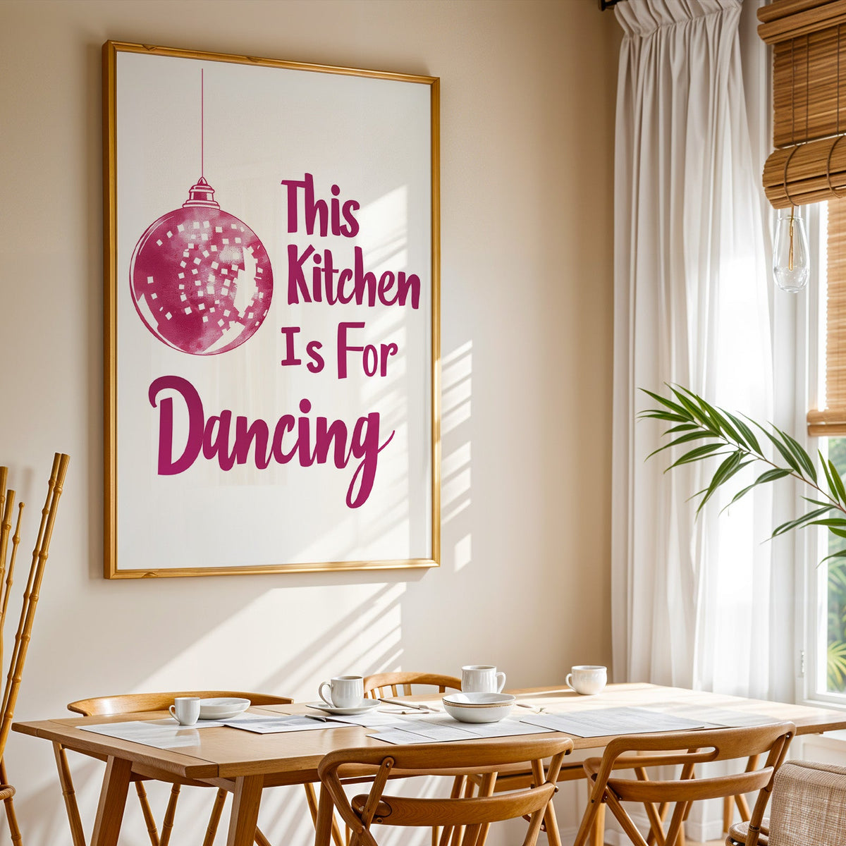 Kitchen Is For Dancing pink script print shown in a gold frame above a breakfast table by a curtained window