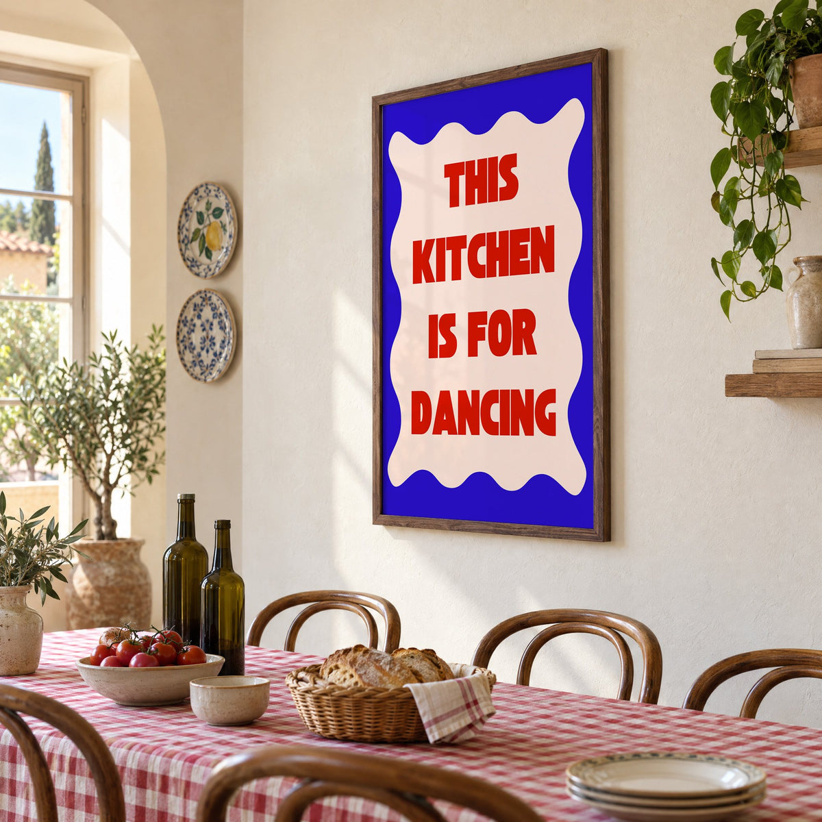 Kitchen Is for Dancing wavy blue print in a walnut frame above a gingham-covered trattoria table, seen at an angle