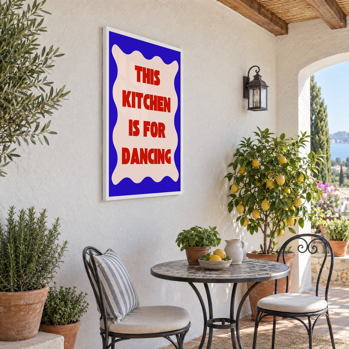 Kitchen Is for Dancing wavy blue print in a white frame on a sunny patio wall beside a potted lemon tree