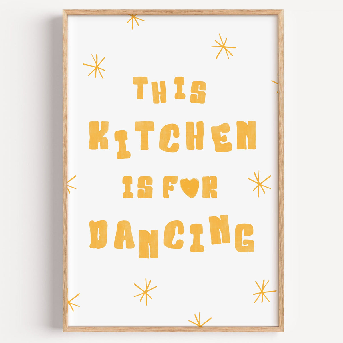 Kitchen Is For Dancing yellow star print in a light oak frame on a plain white wall