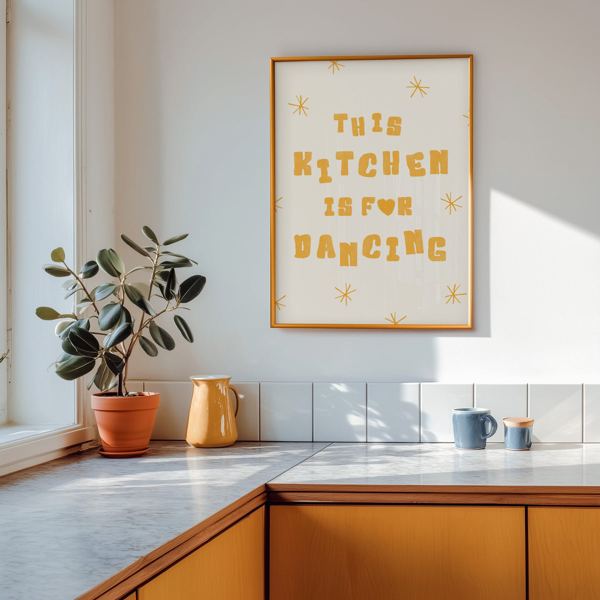Kitchen Is For Dancing yellow star print shown in a gold frame above a marble counter with a yellow ceramic jug