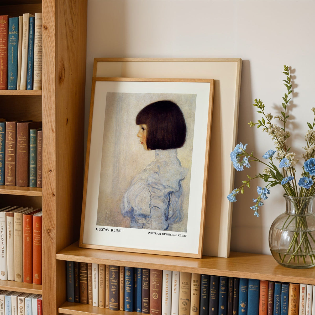 Klimt portrait in an oak frame leaning on a bookshelf beside blue flowers