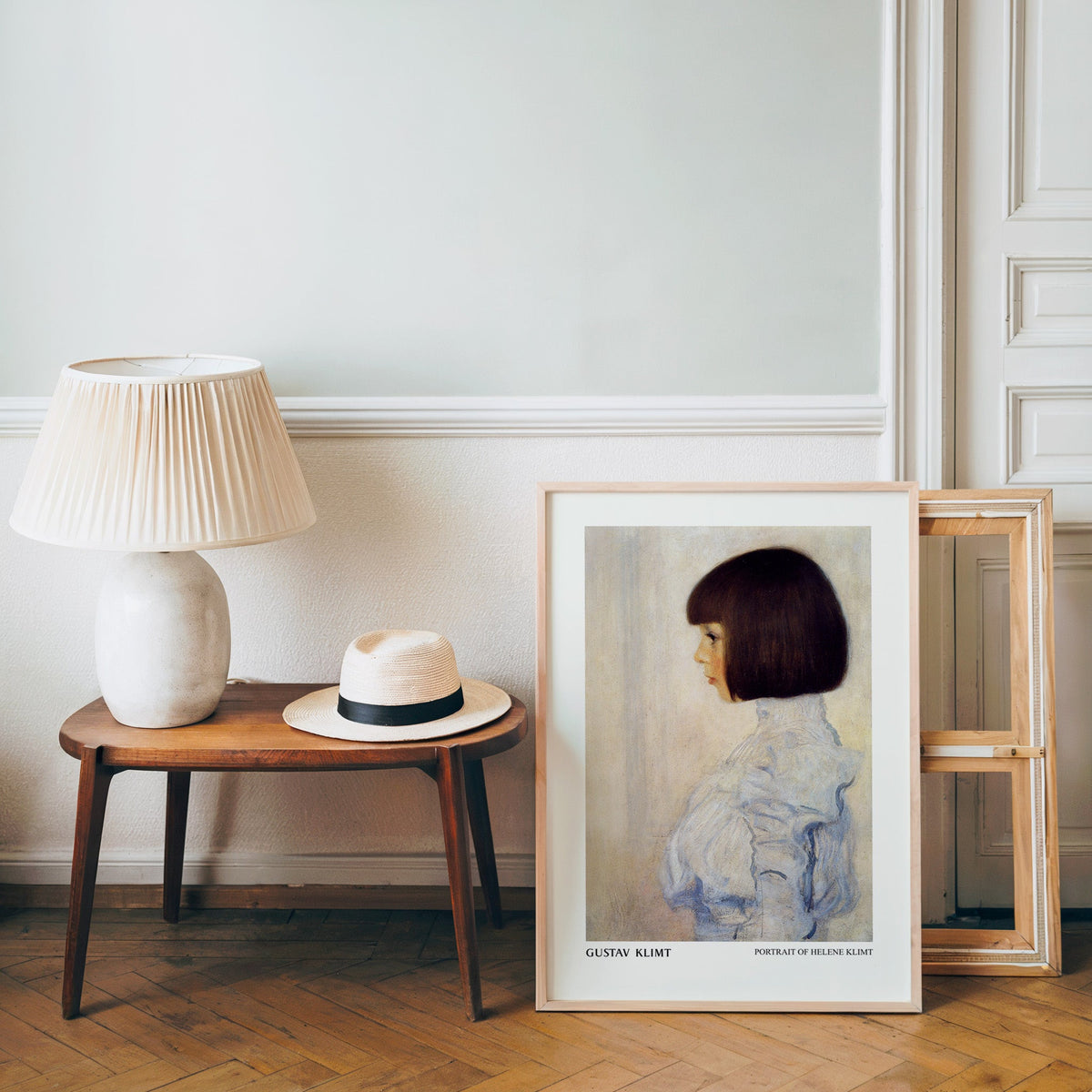 Klimt poster in a light wood frame leaning by a bench and panama hat