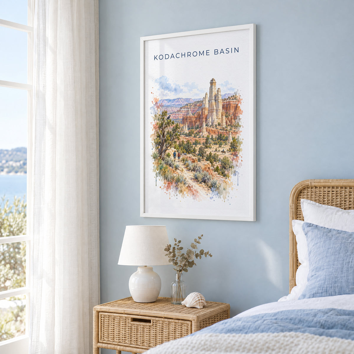 Kodachrome Basin State Park watercolor print in a white frame on a pale blue wall beside a rattan bed in a coastal bedroom
