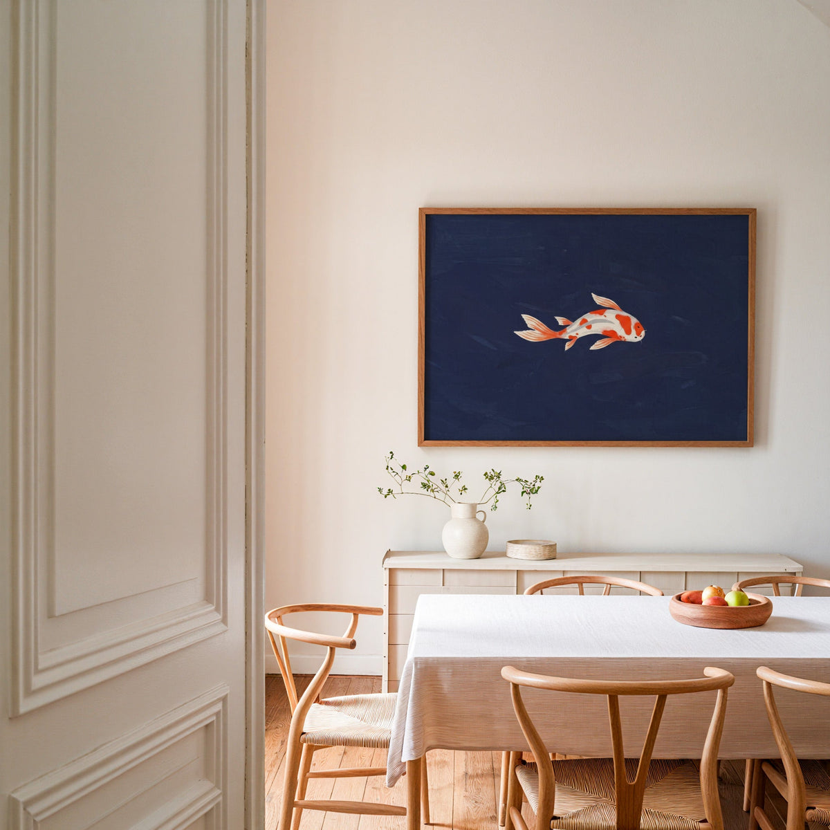 Navy koi wall art print in an oak frame in a dining room with wishbone chairs