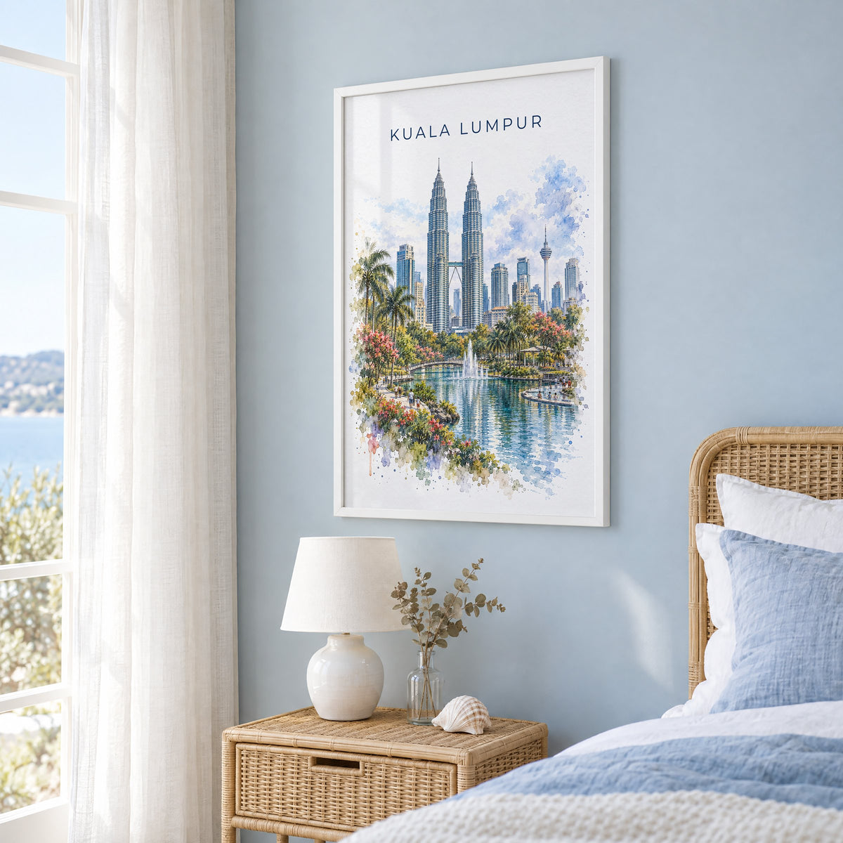 Kuala Lumpur watercolor print in a white frame on a pale blue wall beside a rattan bed in a coastal bedroom