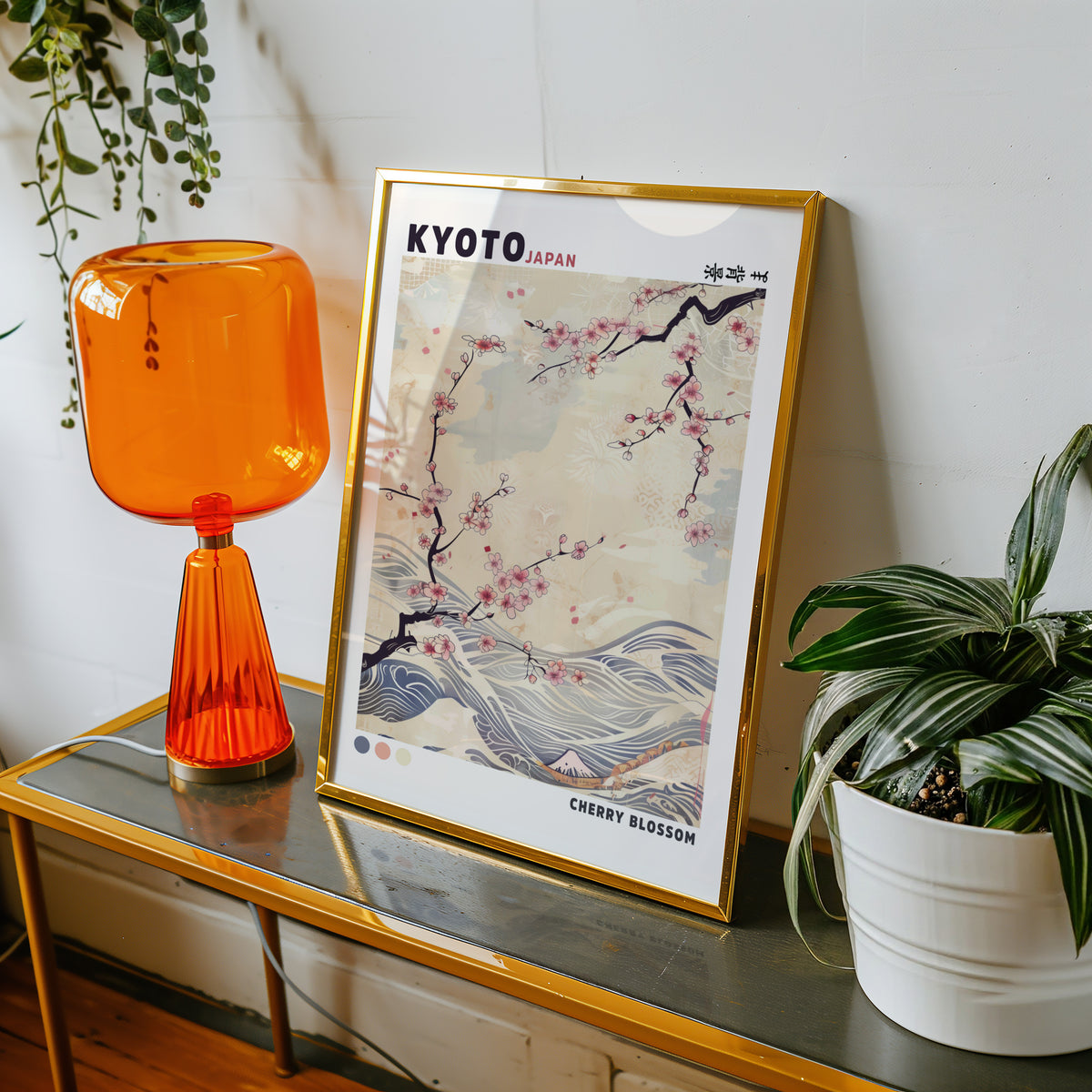 Kyoto cherry blossom and waves print shown in a gold frame on a console beside an orange glass lamp
