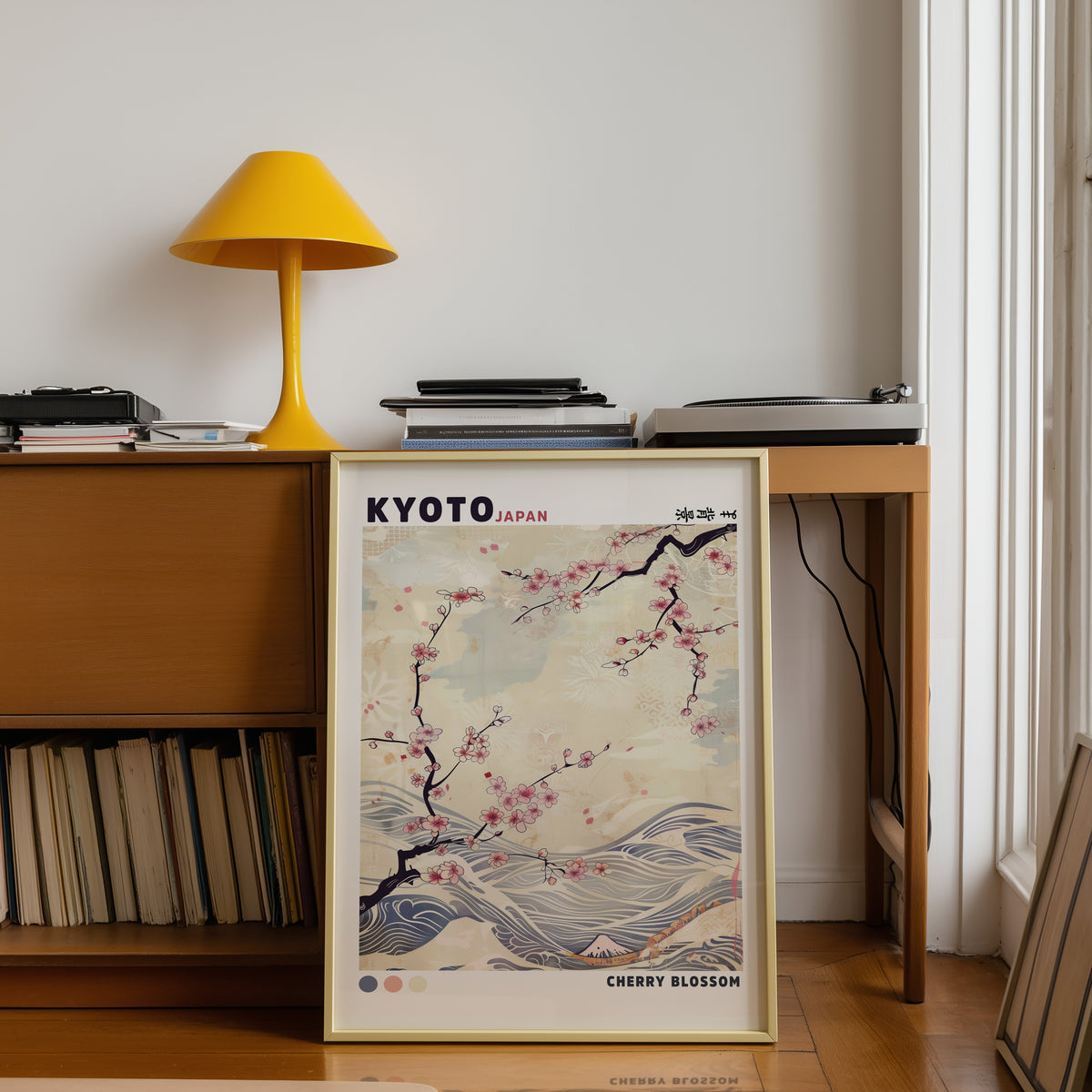 Kyoto cherry blossom and waves print shown in a gold frame below a teak desk with a yellow lamp