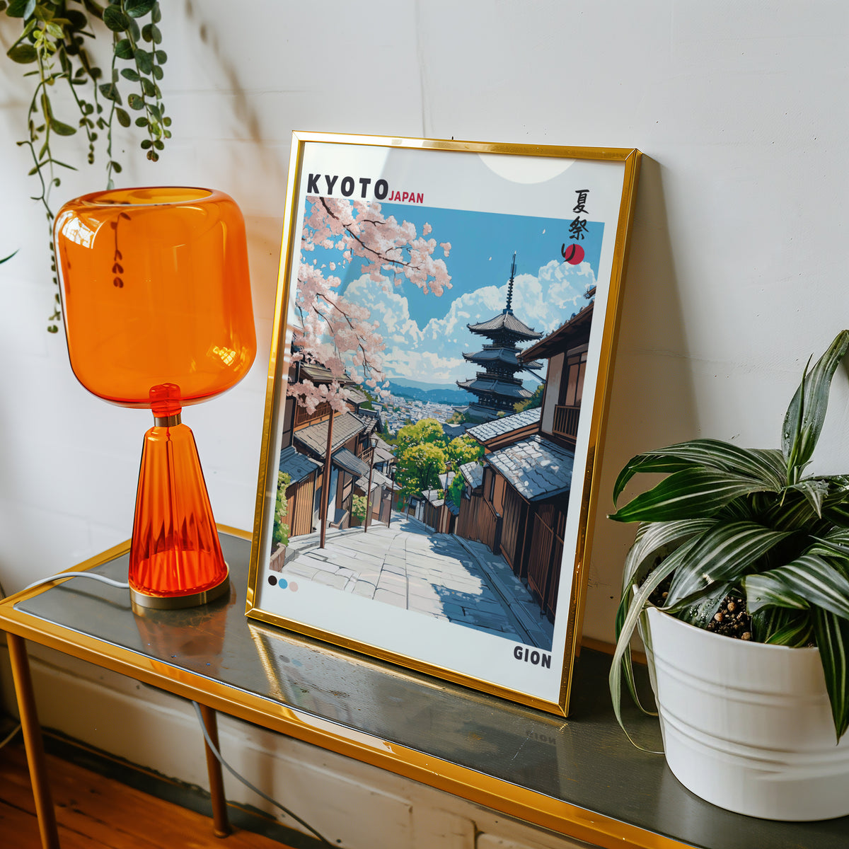Kyoto Gion cherry blossom street print shown in a gold frame on a console beside an orange glass lamp
