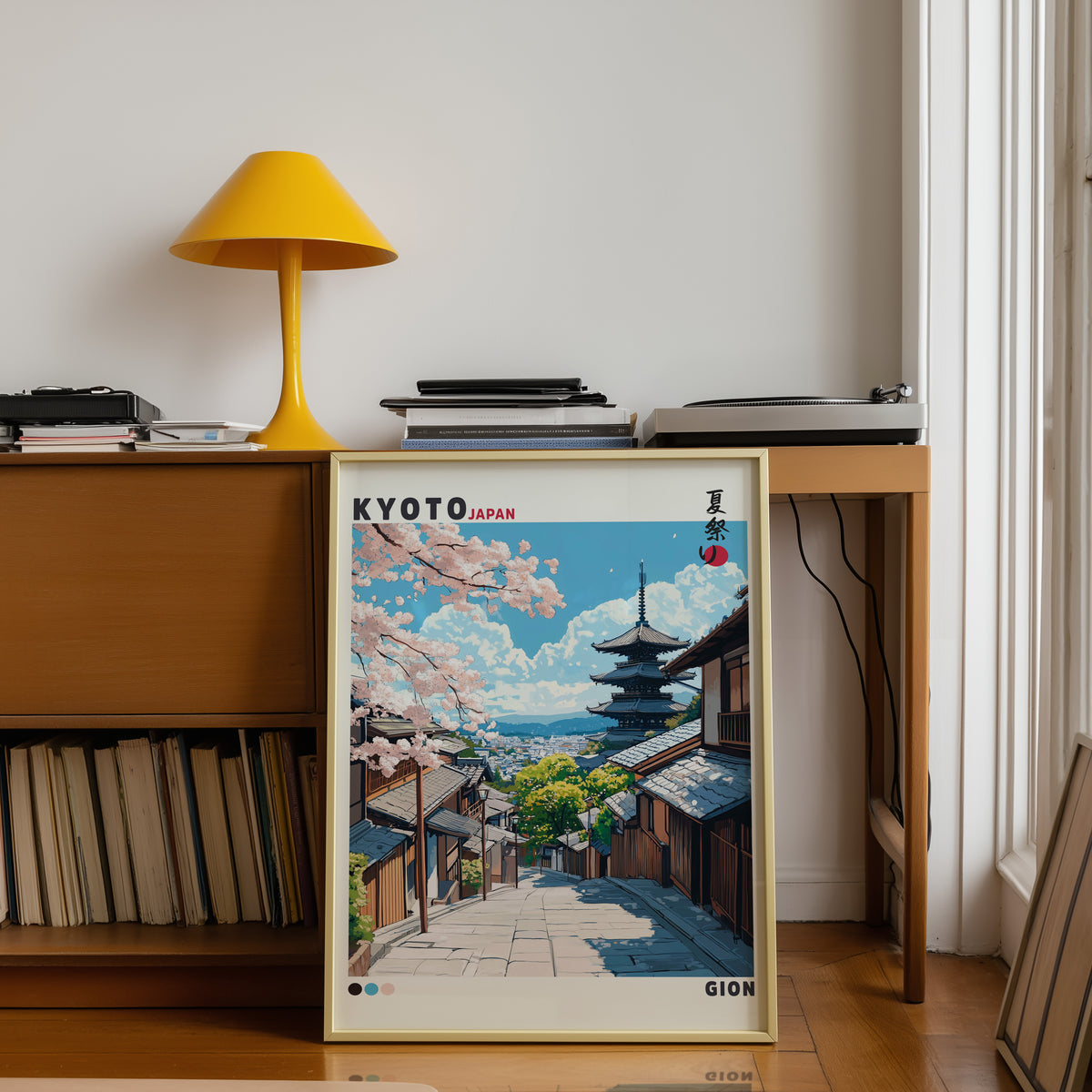 Kyoto Gion cherry blossom street print shown in a gold frame below a teak desk with a yellow lamp