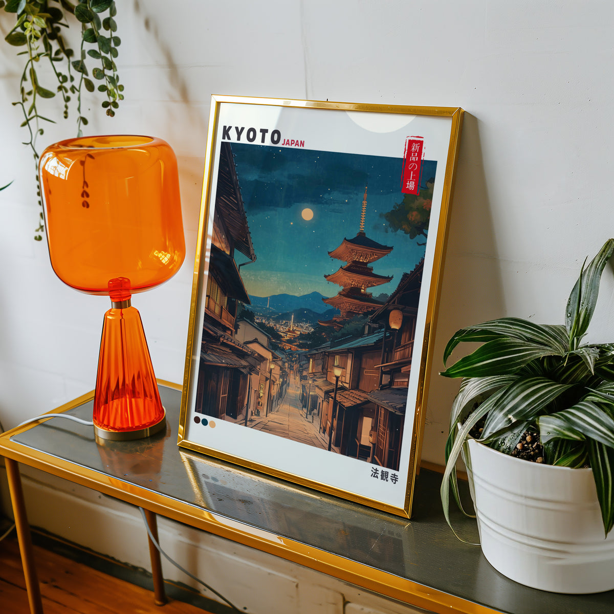 Kyoto night street and Yasaka pagoda print shown in a gold frame on a console beside an orange glass lamp