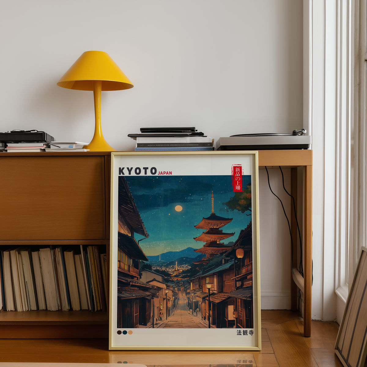 Kyoto night street and Yasaka pagoda print shown in a gold frame below a teak desk with a yellow lamp