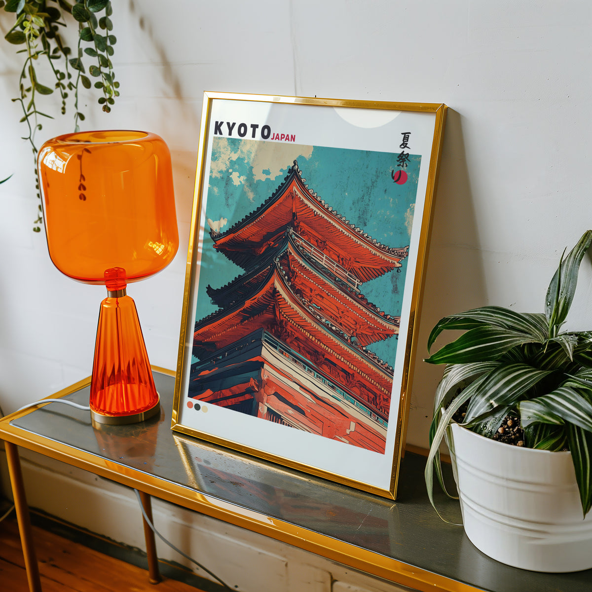 Red pagoda roofs under teal sky print shown in a gold frame on a console beside an orange glass lamp