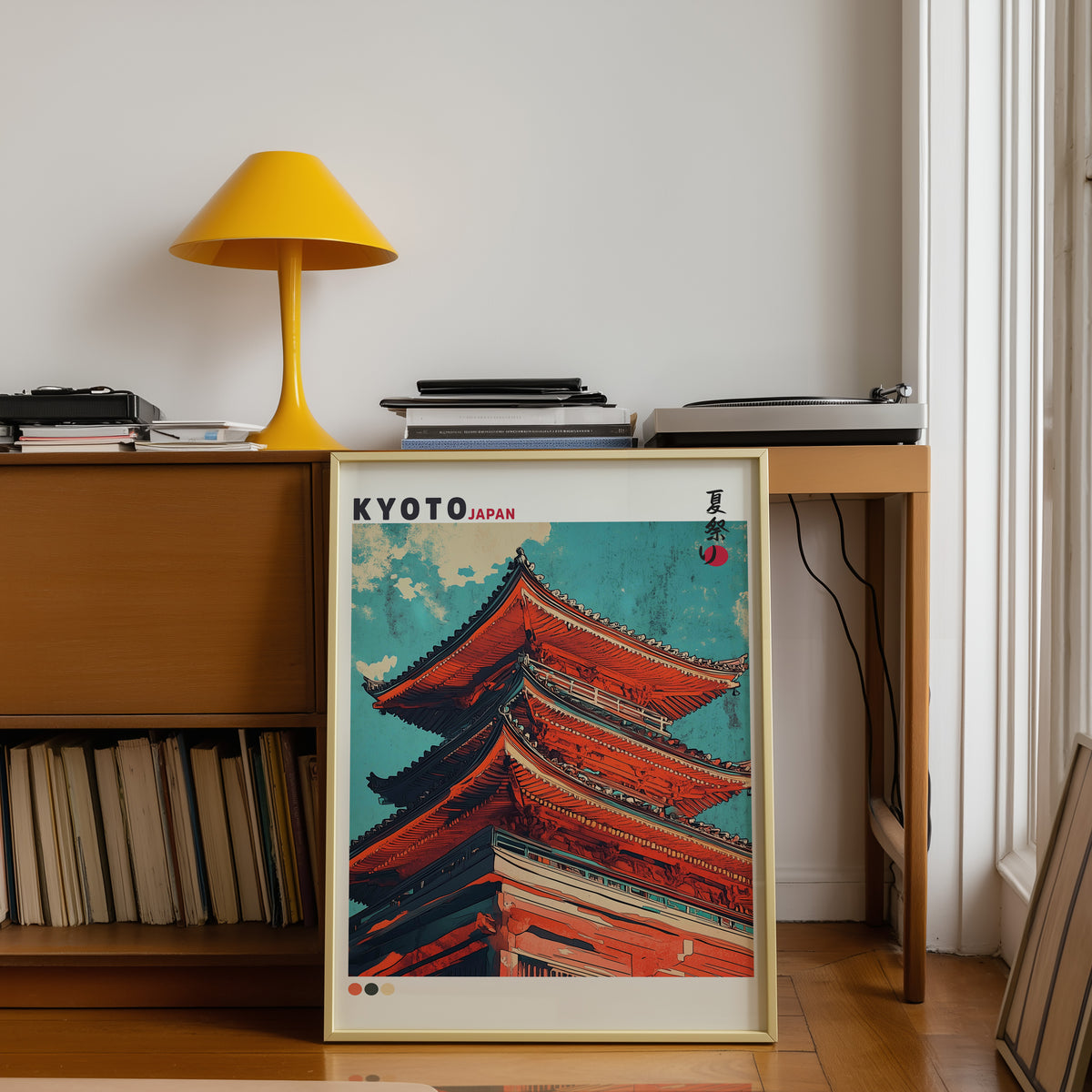 Red pagoda roofs under teal sky print shown in a gold frame below a teak desk with a yellow lamp