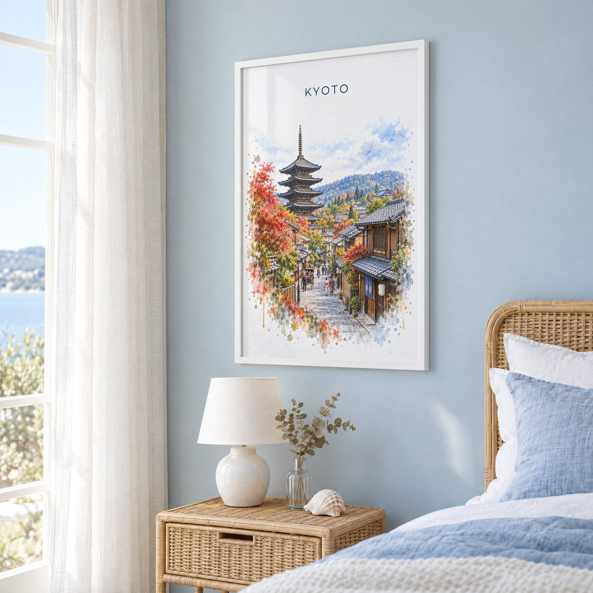 Kyoto watercolor print in a white frame on a pale blue wall beside a rattan bed in a coastal bedroom
