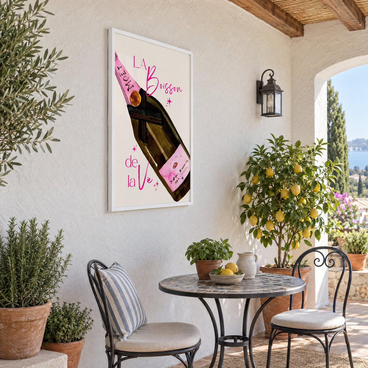 La Boisson champagne bottle watercolor print in a white frame on a sunny patio wall beside a potted lemon tree