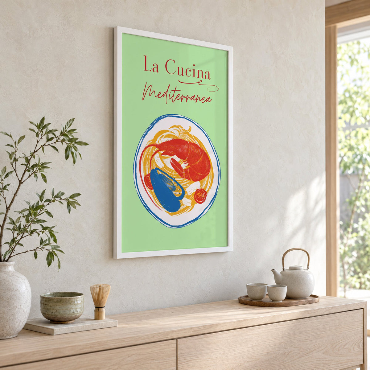 La Cucina Mediterranea seafood pasta print in a white frame above a pale wood console with a matcha tea set