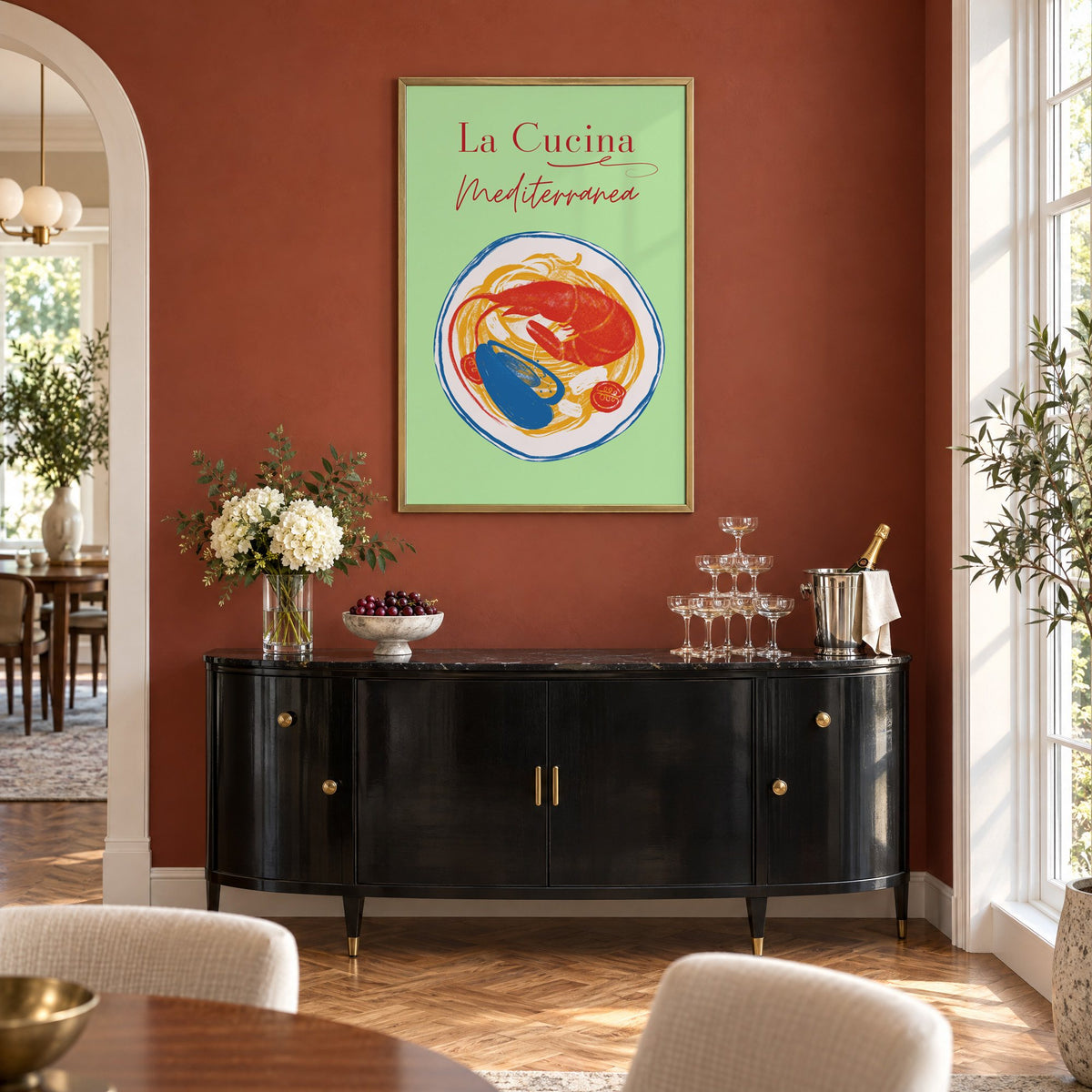 La Cucina Mediterranea seafood pasta print in a brass frame on a terracotta wall above a black buffet with a champagne tower