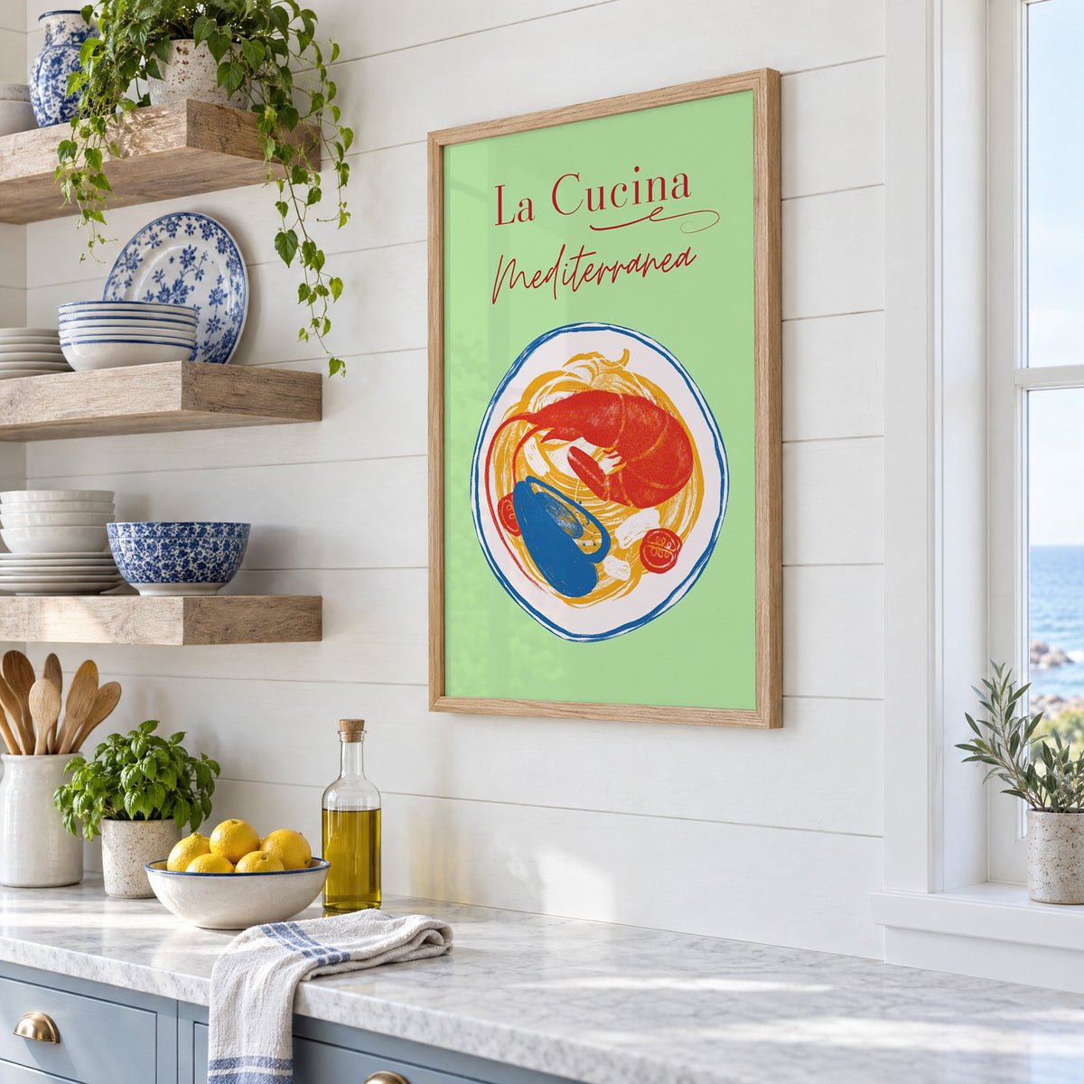 La Cucina Mediterranea seafood pasta print in an oak frame in a white coastal kitchen beside blue and white plates