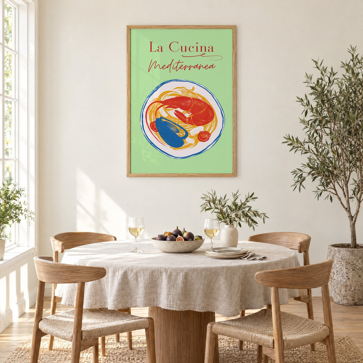 La Cucina Mediterranea seafood pasta print in an oak frame above a round linen-covered dining table with figs and wine