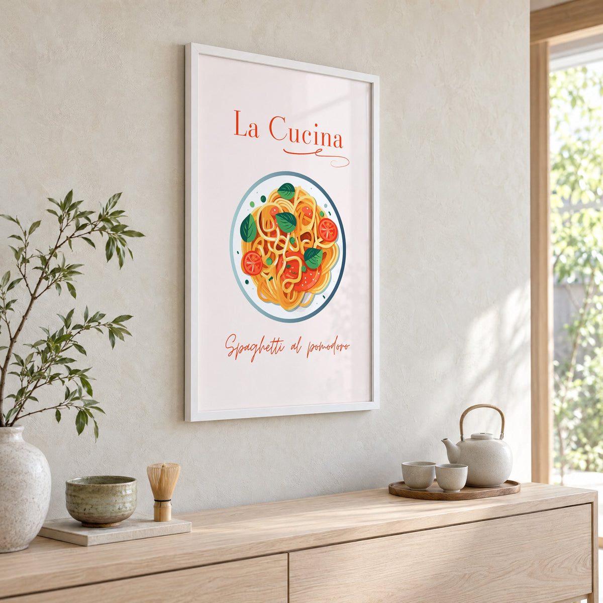 La Cucina spaghetti plate print in a white frame above a pale wood console with a matcha tea set