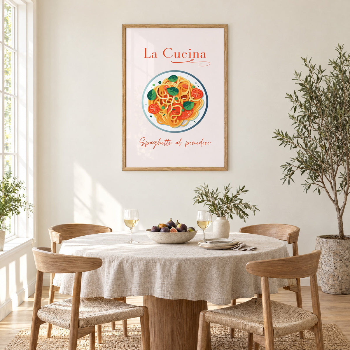 La Cucina spaghetti plate print in an oak frame above a round linen-covered dining table with figs and wine