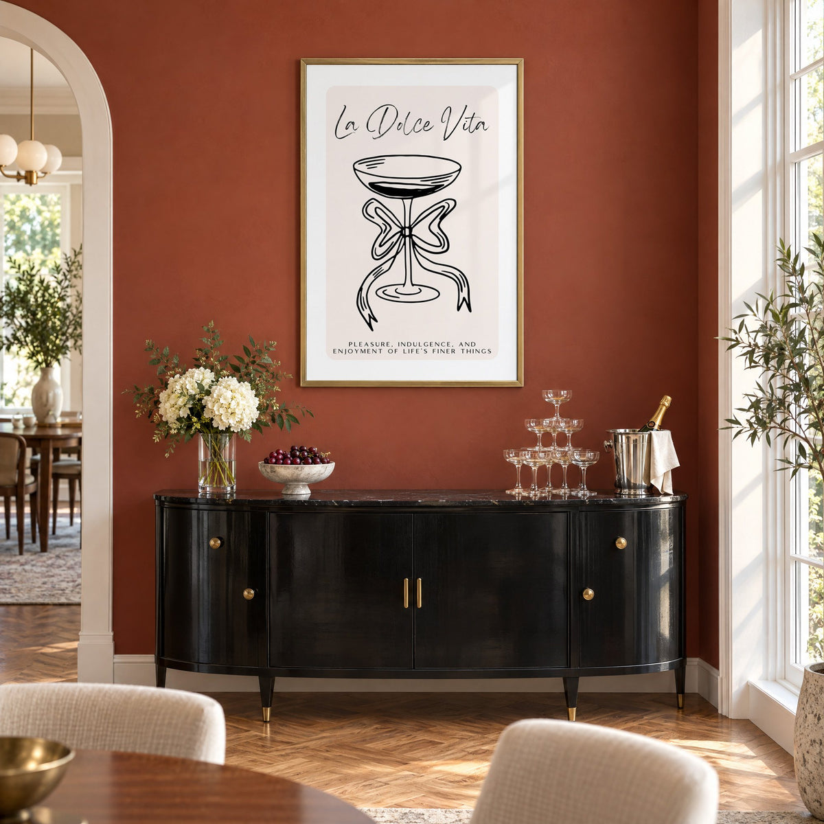 La Dolce Vita black line coupe print in a brass frame on a terracotta wall above a black buffet with a champagne tower