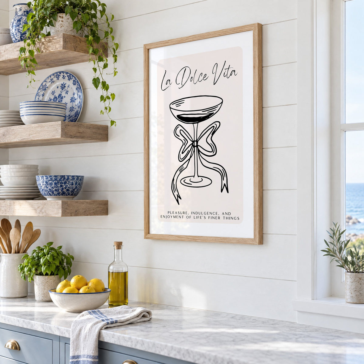 La Dolce Vita black line coupe print in an oak frame in a white coastal kitchen beside blue and white plates