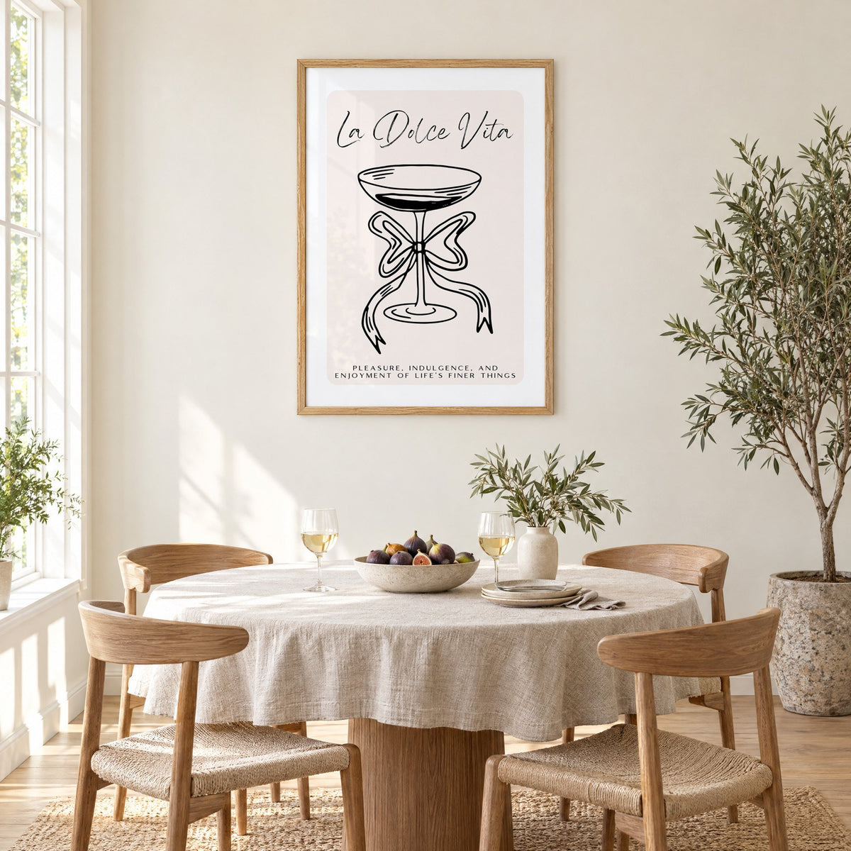 La Dolce Vita black line coupe print in an oak frame above a round linen-covered dining table with figs and wine