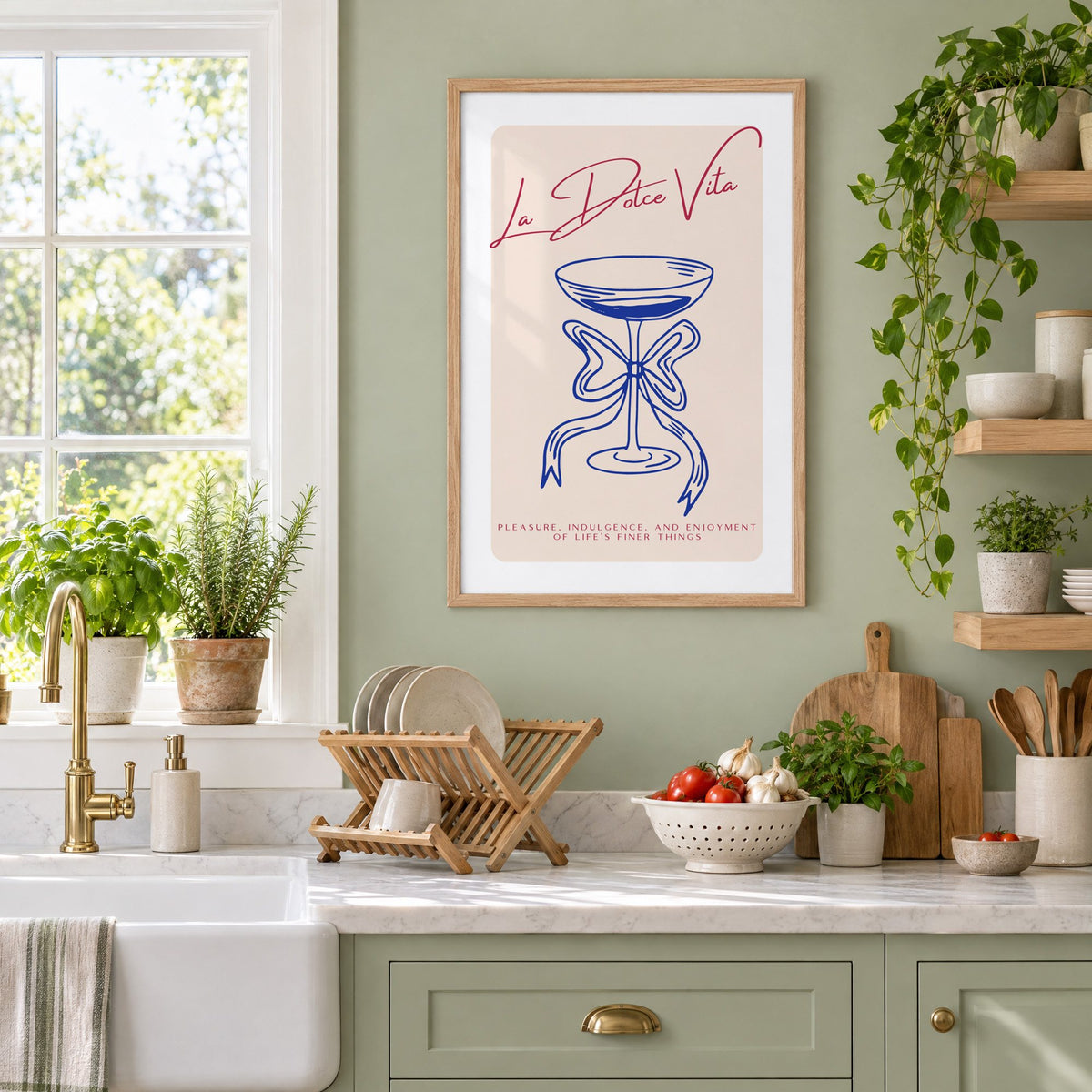 La Dolce Vita cobalt coupe print in an oak frame on a sage green kitchen wall beside a farmhouse sink and herbs