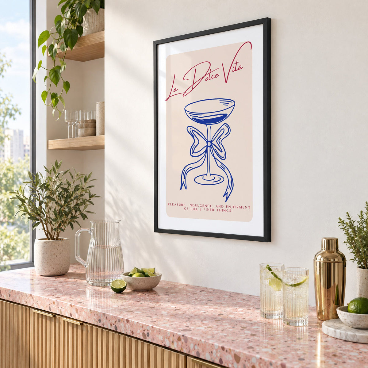 La Dolce Vita cobalt coupe print in a black frame above a pink terrazzo cocktail counter with limes, seen at an angle