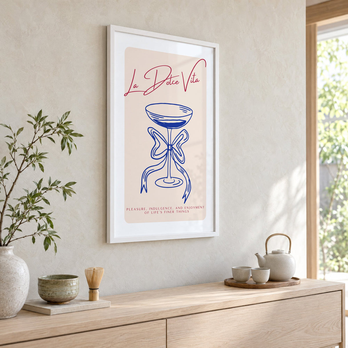 La Dolce Vita cobalt coupe print in a white frame above a pale wood console with a matcha tea set