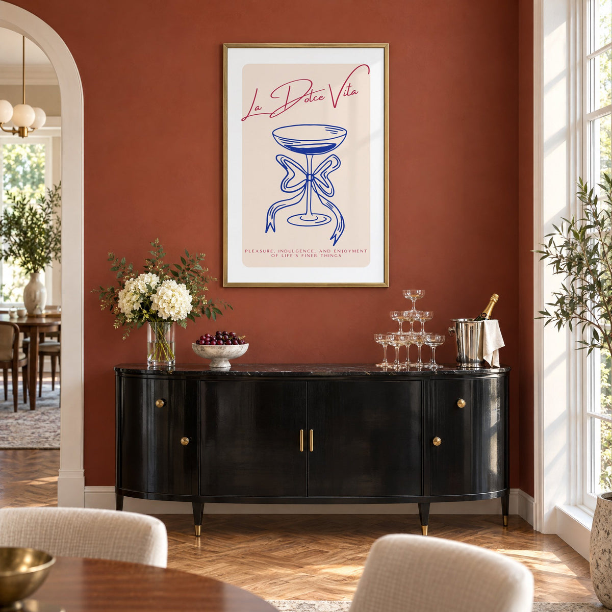La Dolce Vita cobalt coupe print in a brass frame on a terracotta wall above a black buffet with a champagne tower