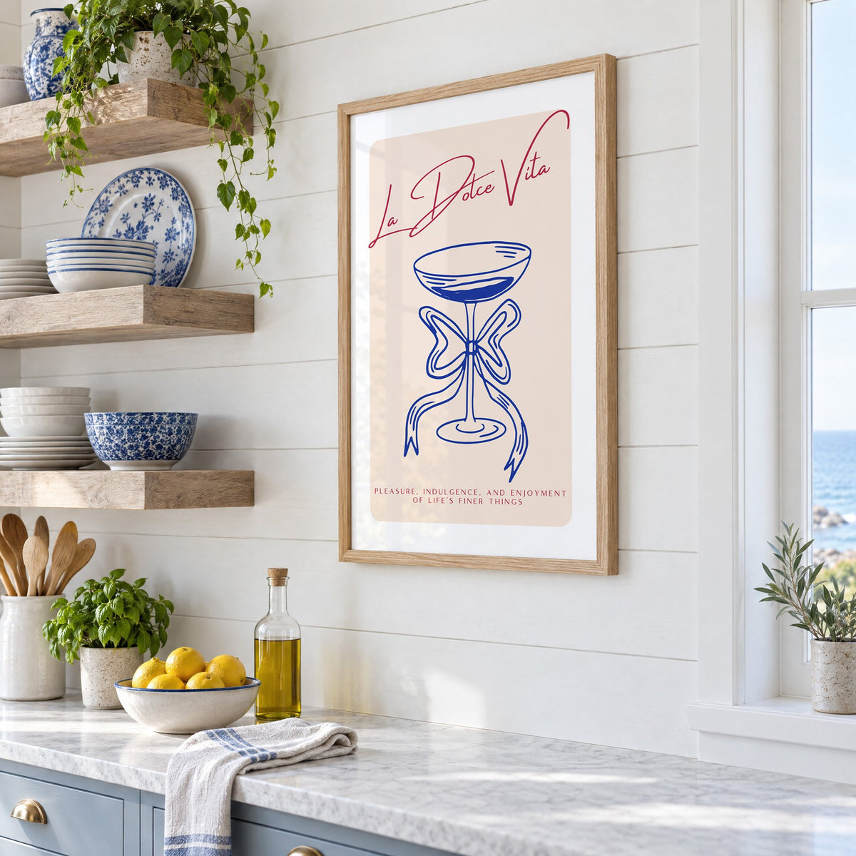 La Dolce Vita cobalt coupe print in an oak frame in a white coastal kitchen beside blue and white plates