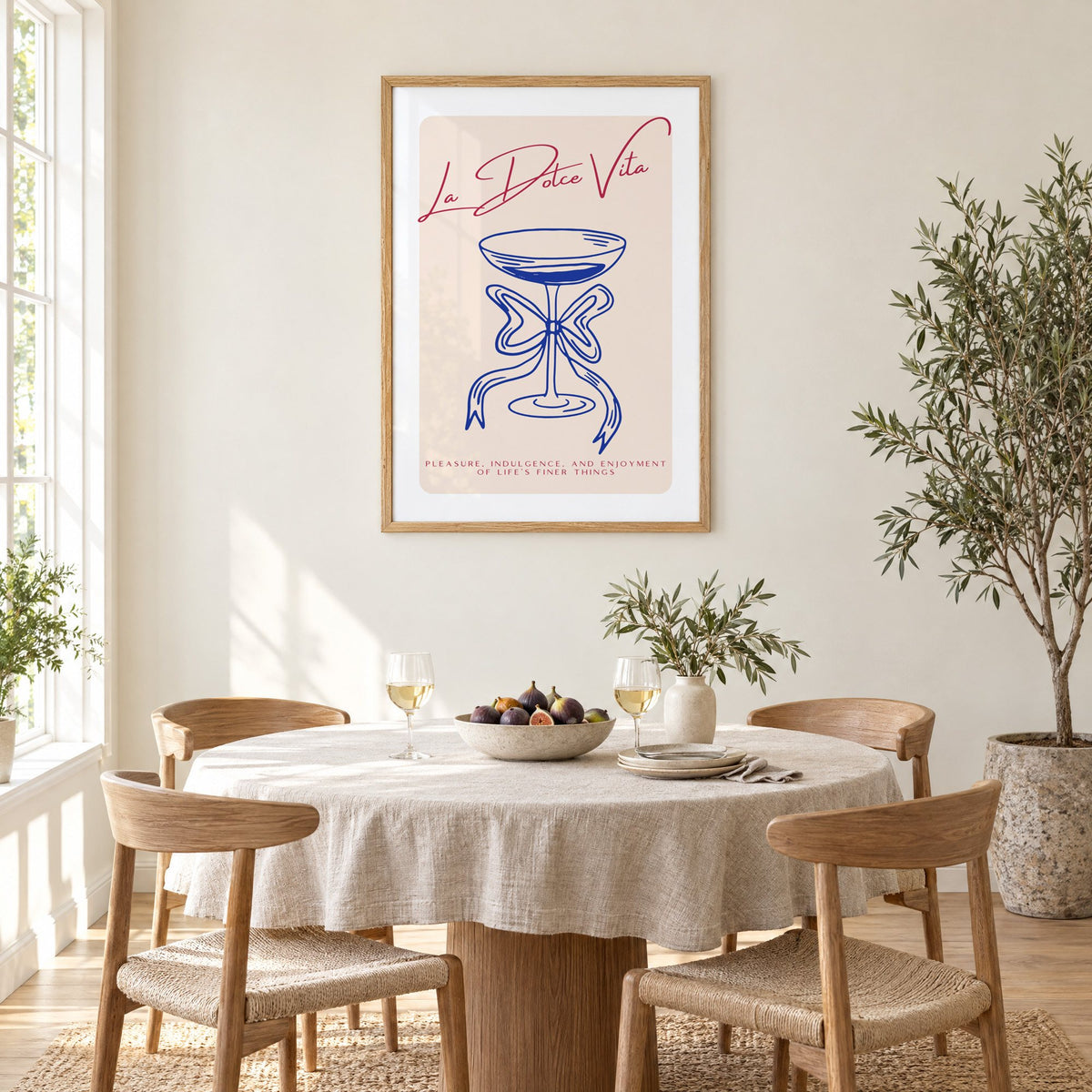La Dolce Vita cobalt coupe print in an oak frame above a round linen-covered dining table with figs and wine