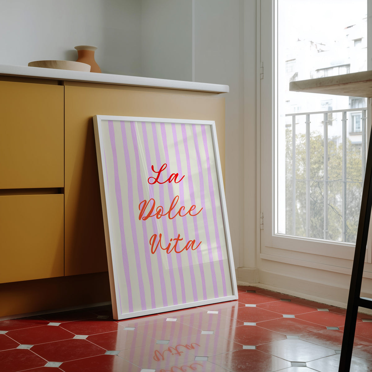 La Dolce Vita print in a white frame against yellow cabinets on a red tiled floor