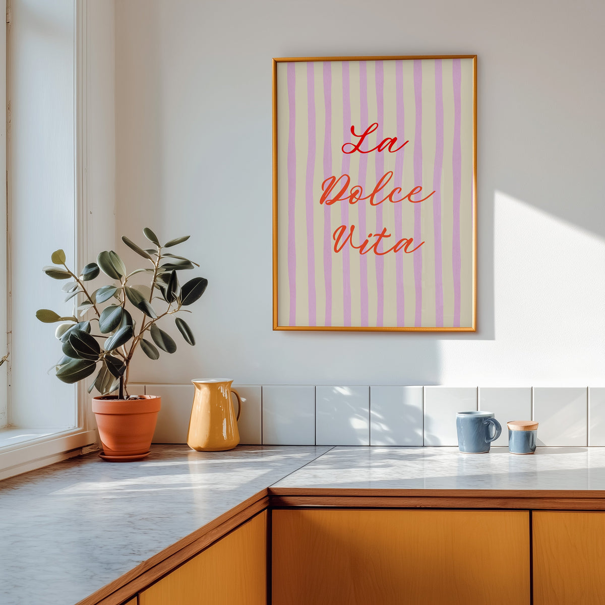 La Dolce Vita print shown in a gold frame above a marble counter with a yellow ceramic jug