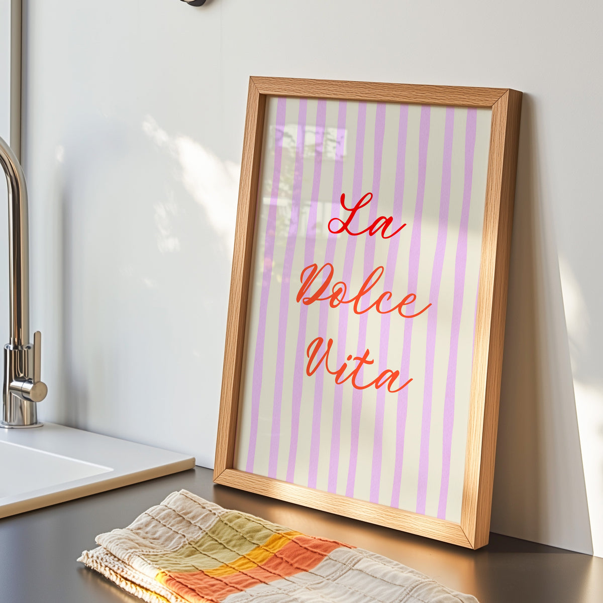 La Dolce Vita print in an oak frame by the kitchen sink beside a striped tea towel