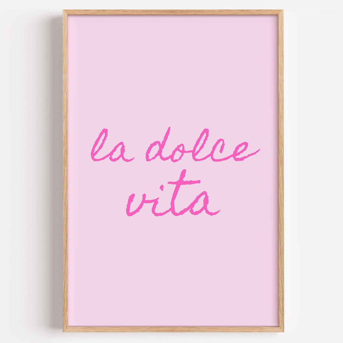la dolce vita pink handwritten script print in a light oak frame on a plain white wall