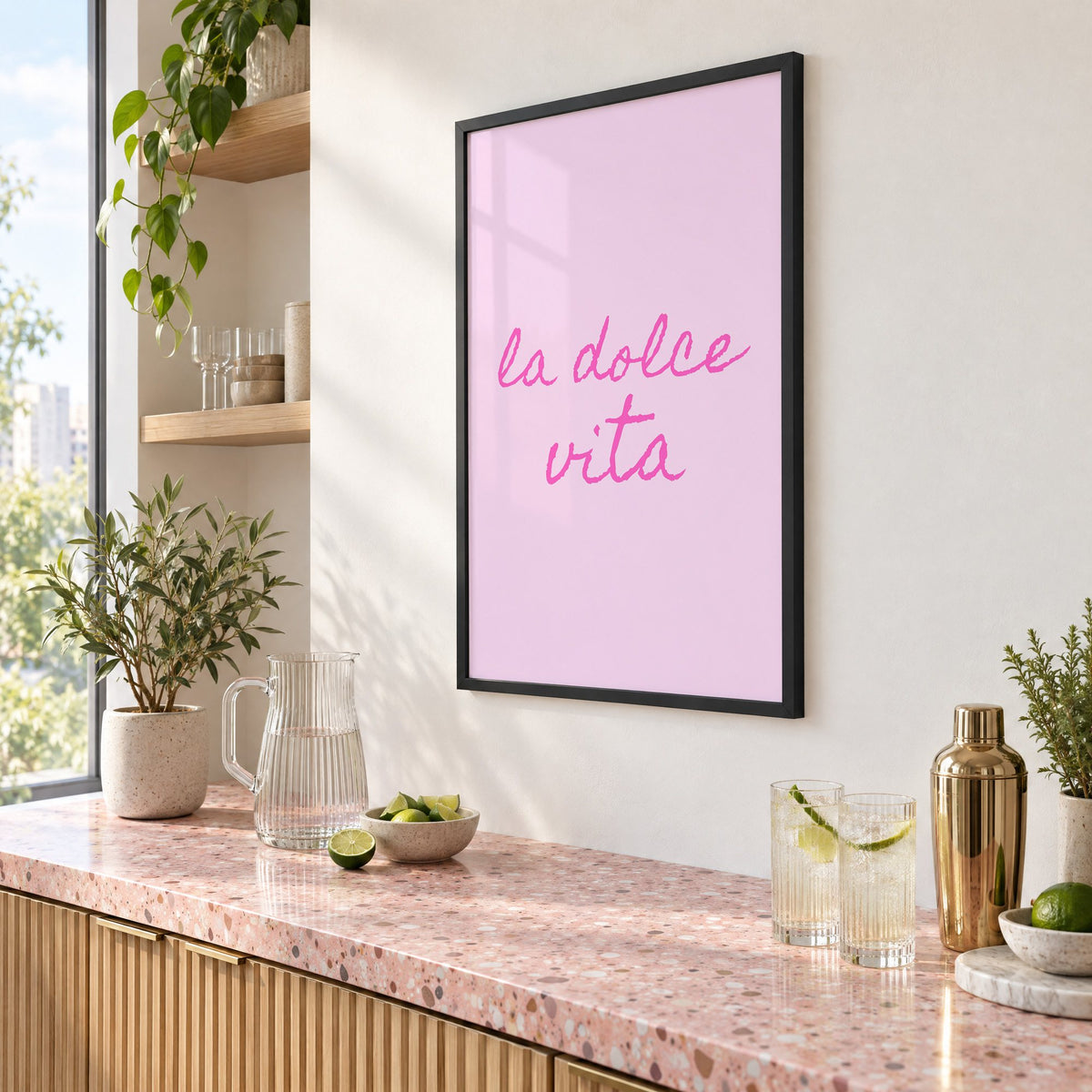 la dolce vita pink handwritten script print in a black frame above a pink terrazzo cocktail counter with limes, seen at an angle