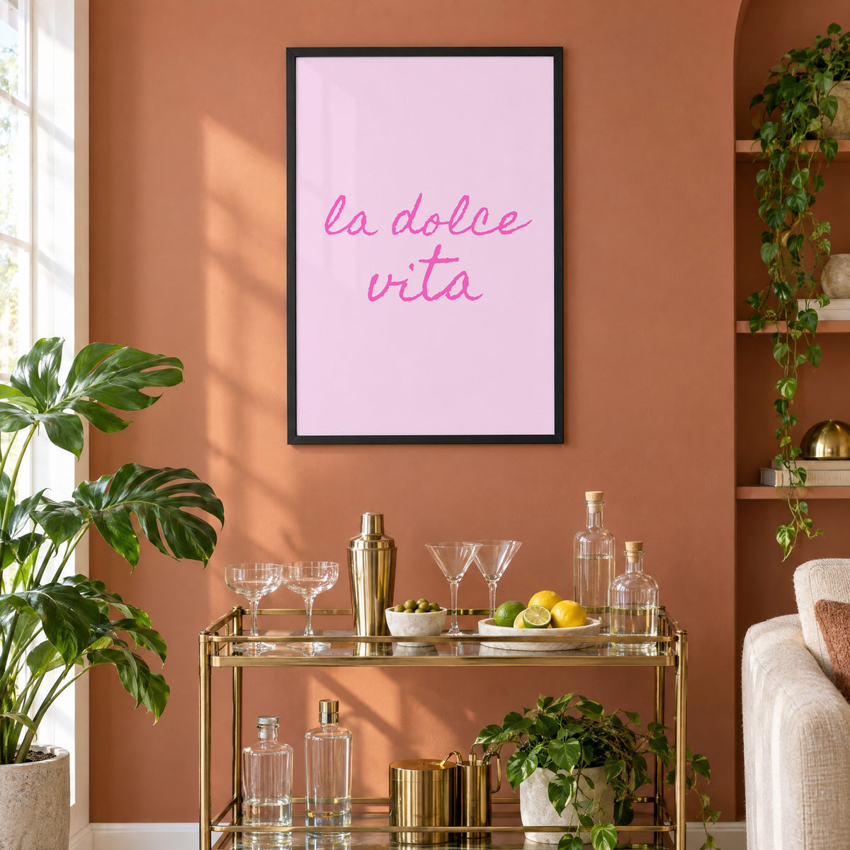 la dolce vita pink handwritten script print in a black frame on a terracotta wall above a brass bar cart with coupes and citrus