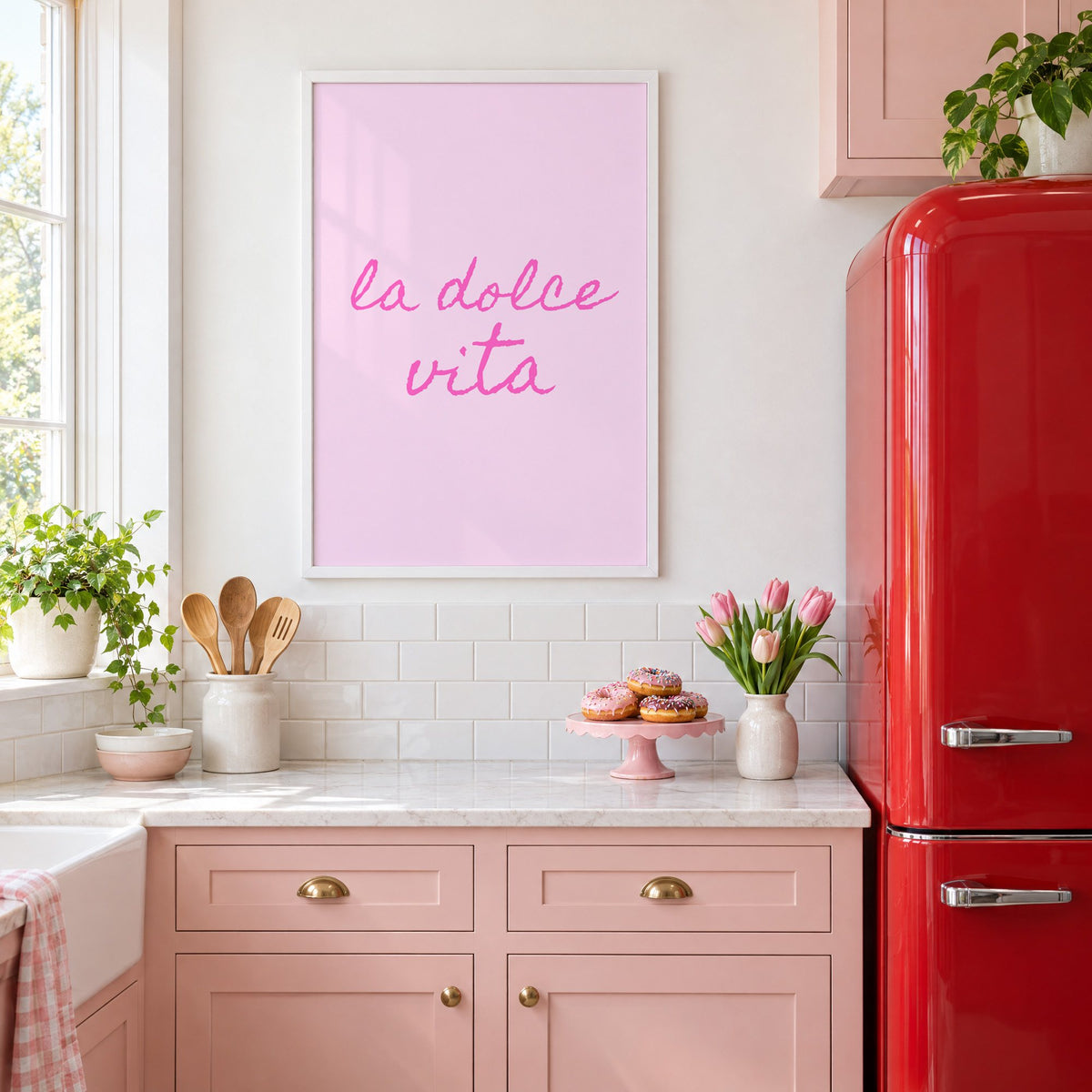 la dolce vita pink handwritten script print in a white frame above pink cabinets beside a red retro fridge