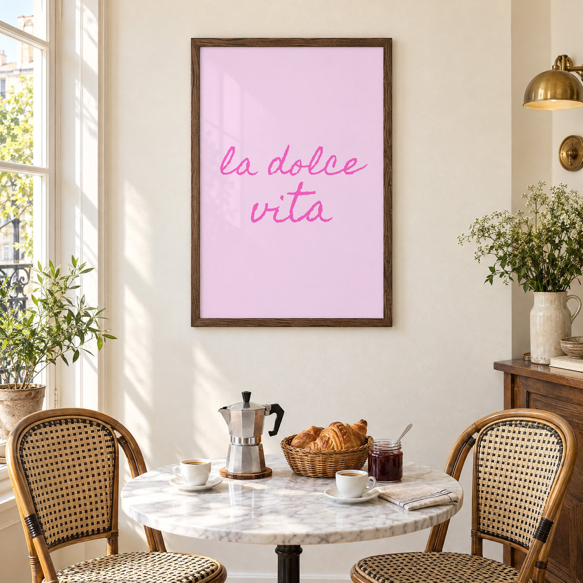la dolce vita pink handwritten script print in a walnut frame above a marble bistro table with croissants and rattan chairs