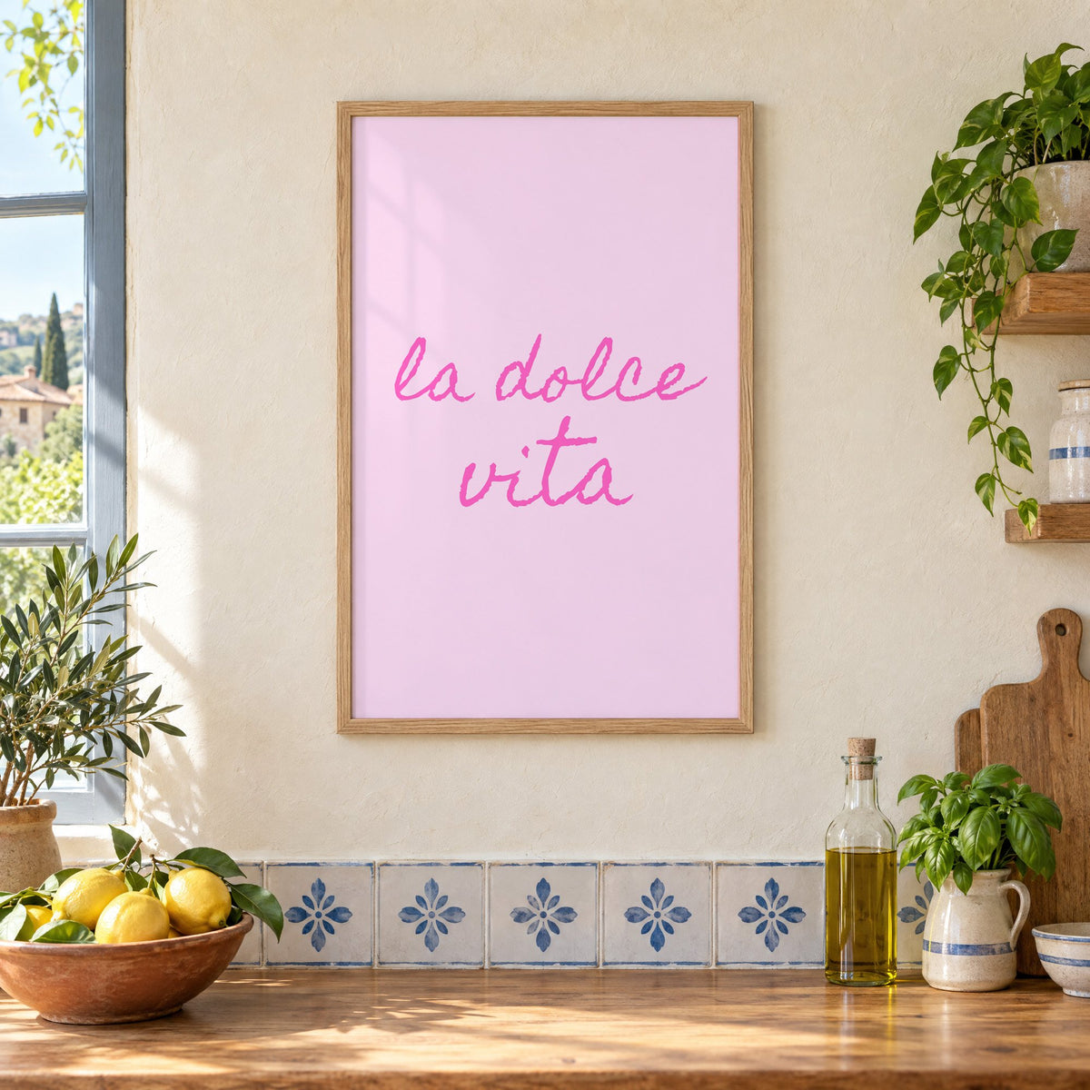 la dolce vita pink handwritten script print in an oak frame on a cream plaster wall above a worktop with a bowl of lemons and blue-and-white tiles