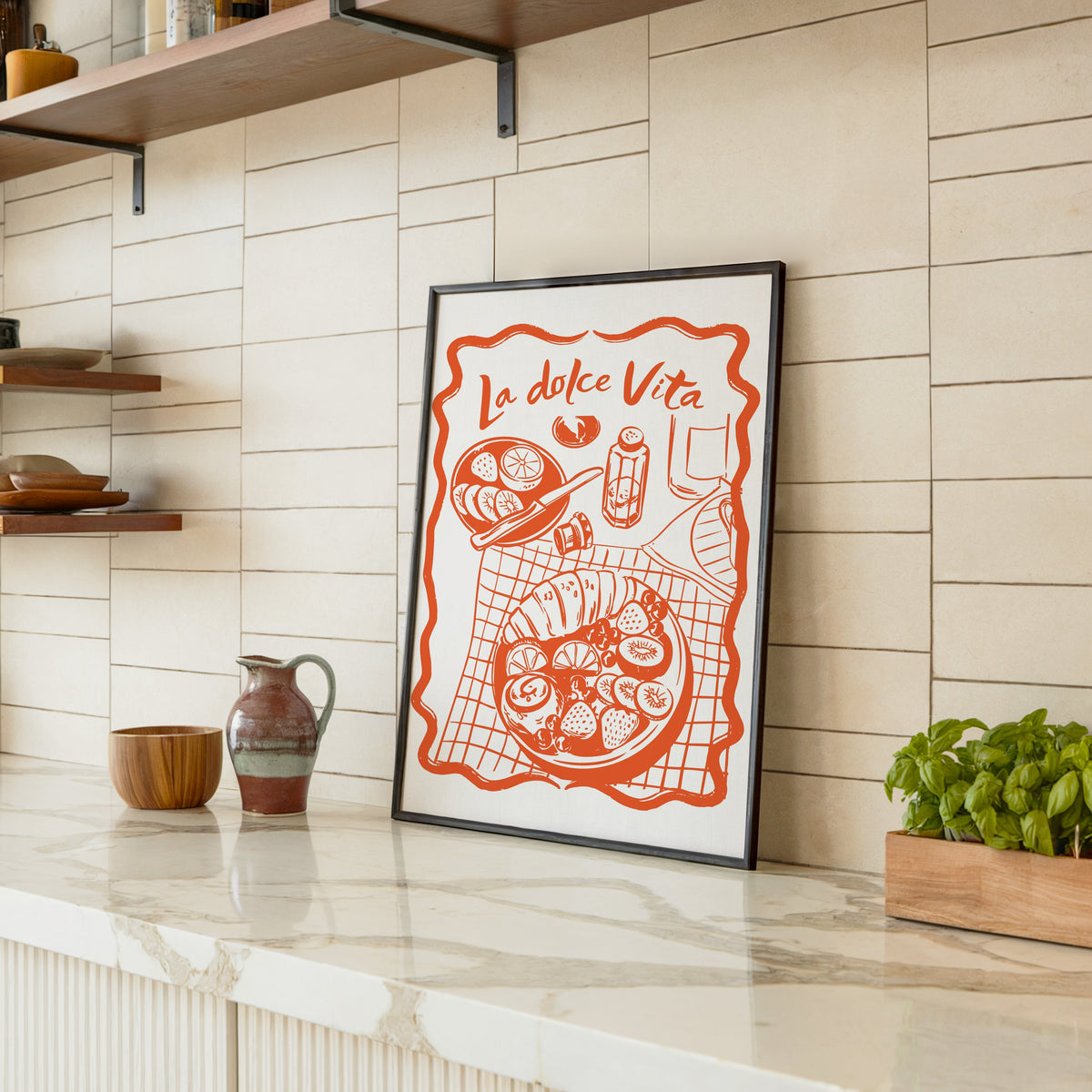 La Dolce Vita table print in a black frame leaning on a marble counter in a tiled kitchen